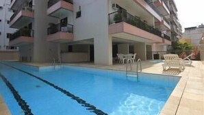 A swimming pool with clear blue water, surrounded by a multi-story building with balconies. - GoHouse Torre do Barao 506 (Rio de Janeiro)