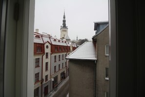 Eine enge Straße mit Häusern an beiden Seiten, im Hintergrund ein markanter Kirchturm und ein Blick durch ein Fenster.