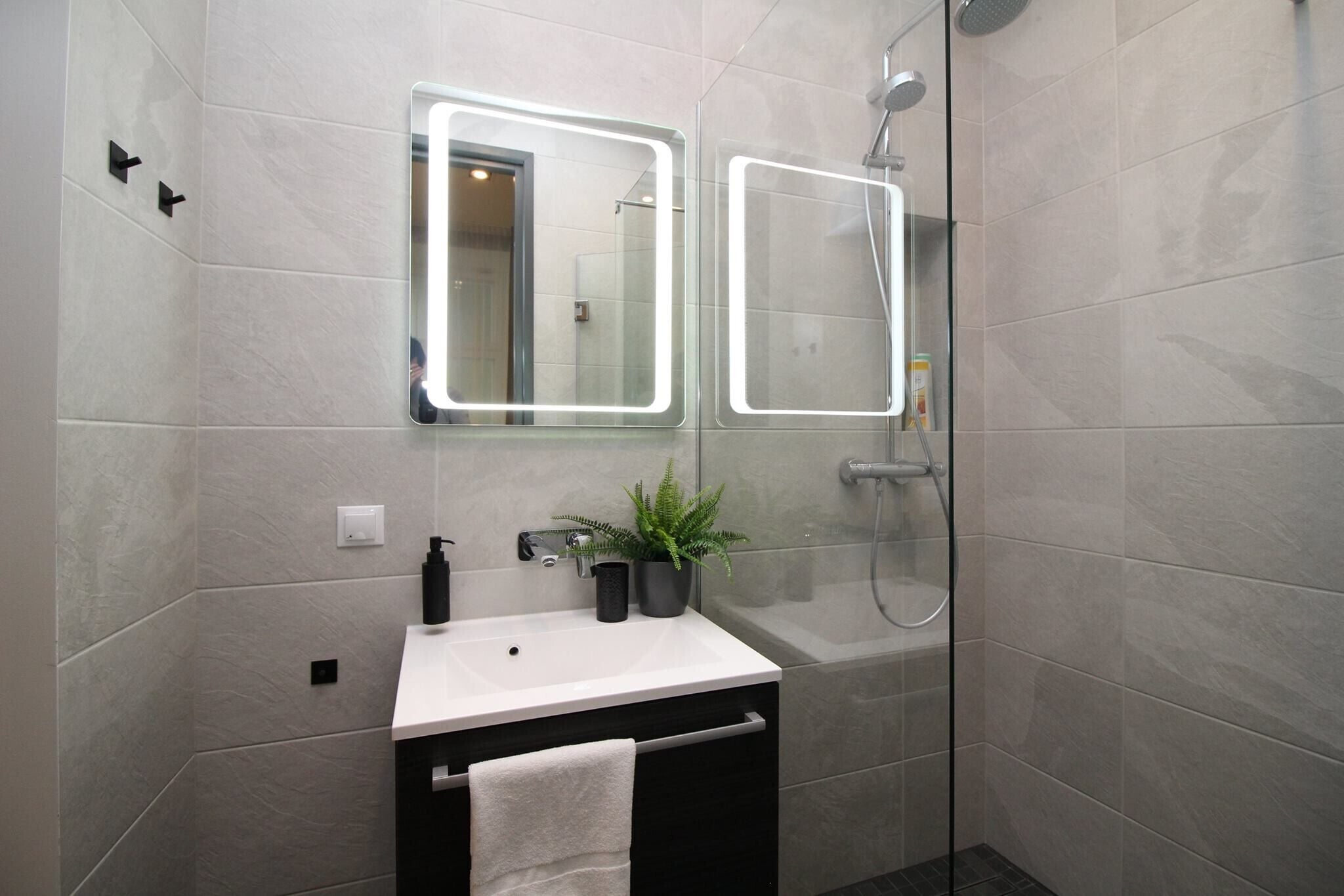 A modern bathroom with a white sink, a mirror, a potted plant, and a shower.