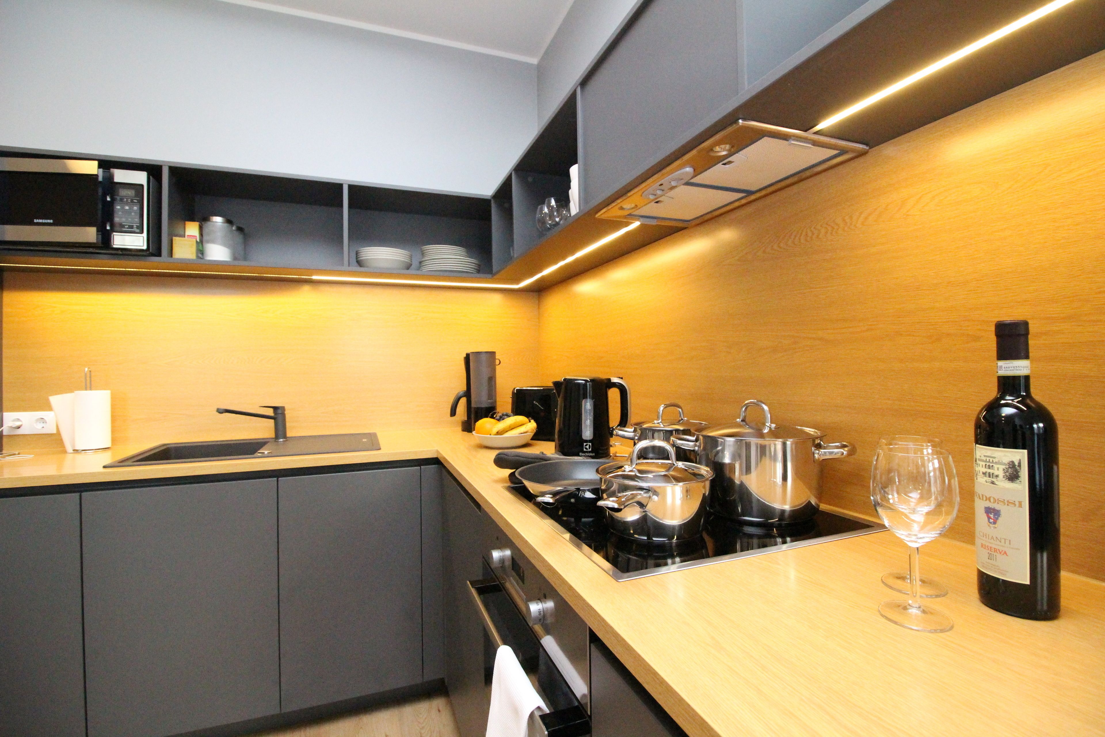 Una cocina moderna con microondas, cafetera, hervidor y botella de vino.