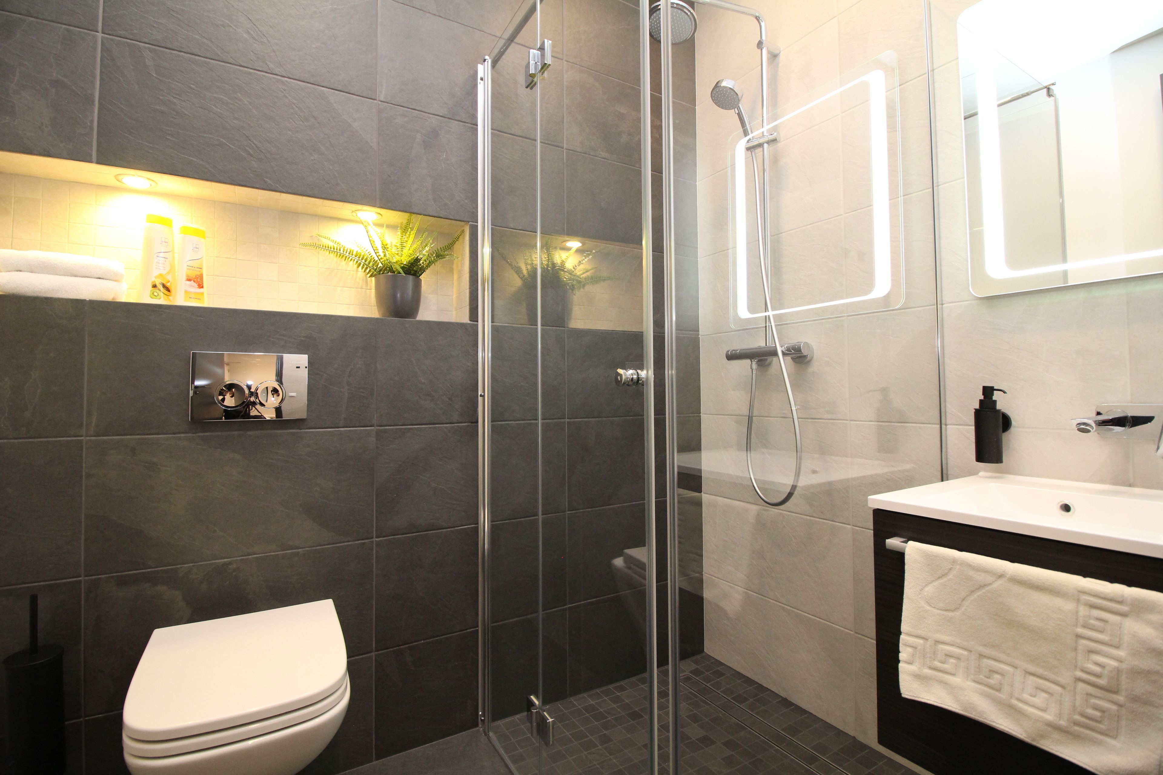A modern bathroom with a glass-enclosed shower, a toilet, a sink with a towel, and a mirror.