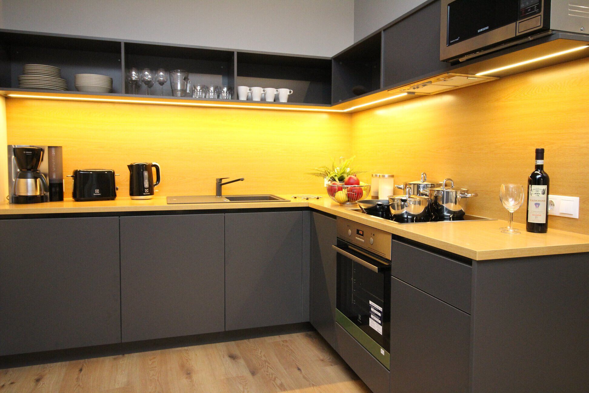 A modern kitchen with a built-in oven, a coffee maker, a kettle, and a wine bottle.