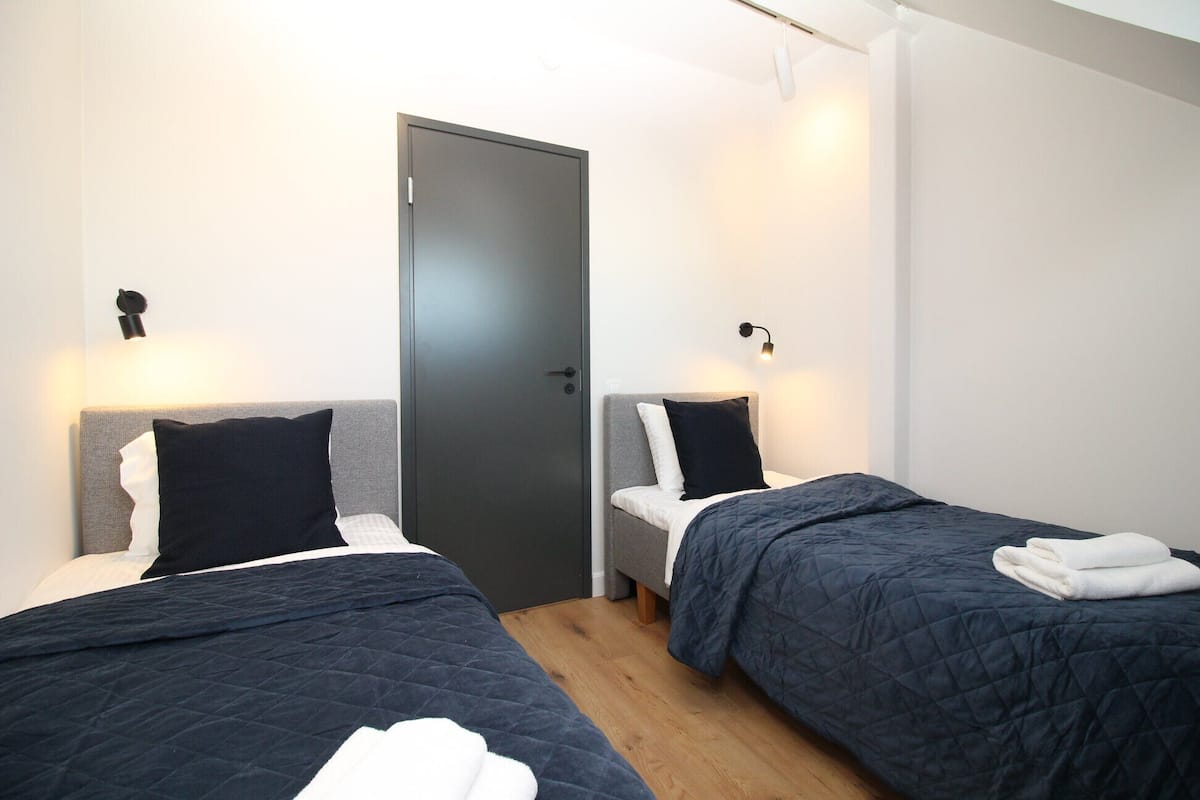 Quarto com duas camas, cada uma com cabeceira, uma porta e luminárias de cabeceira.