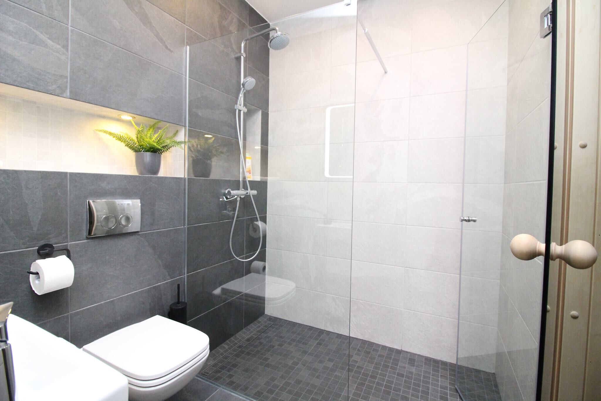 Een moderne badkamer met een douchecabine van glas, een toilet en een wastafel.