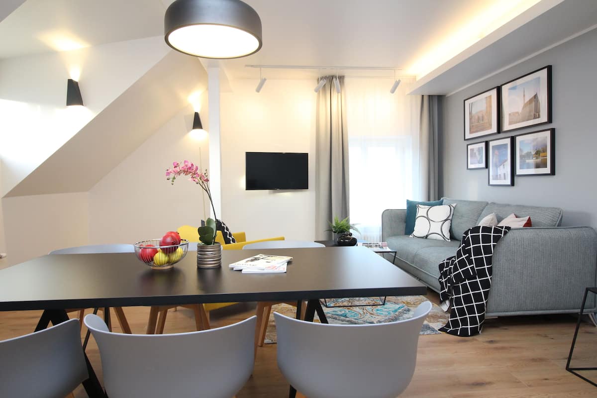 Uma sala de estar moderna com área de jantar, apresentando um sofá, TV de tela plana e quadros nas paredes.