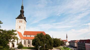 A historic church with a prominent tower and a red roof, surrounded by trees and a paved square.