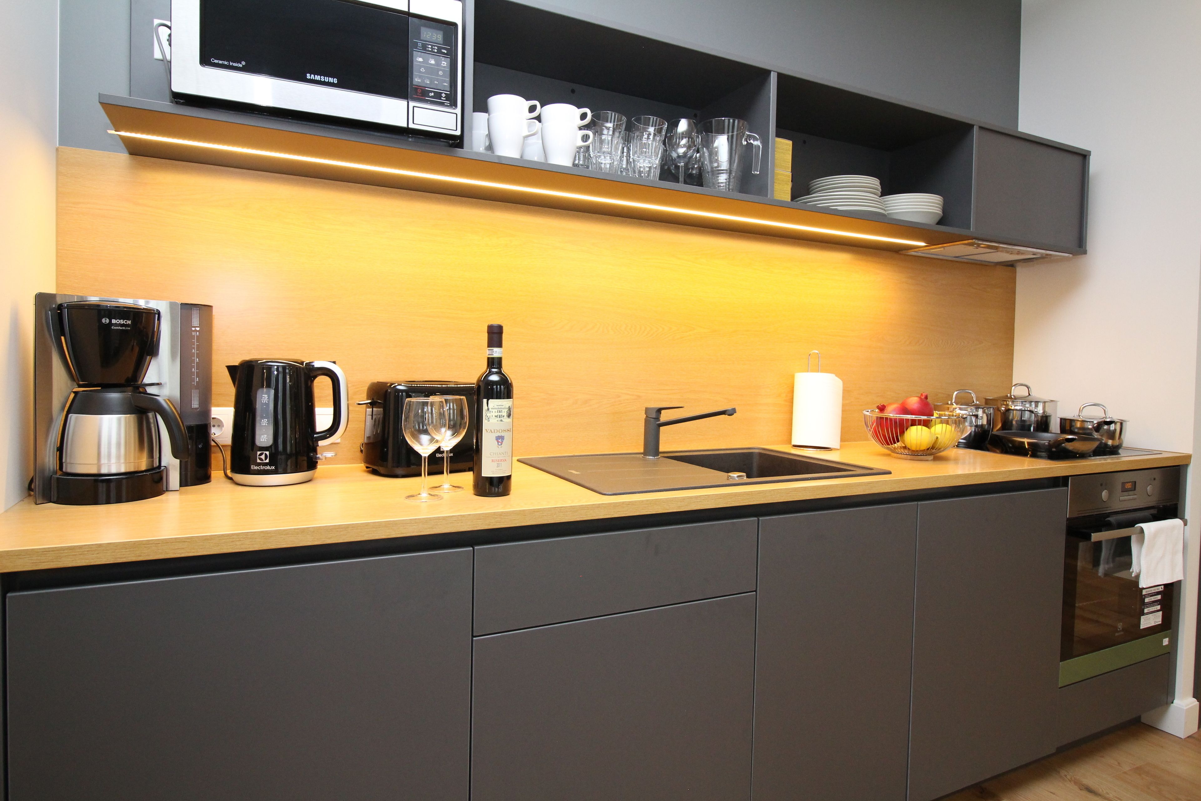 A modern kitchen with a microwave, coffee maker, wine bottle, and various kitchen utensils.