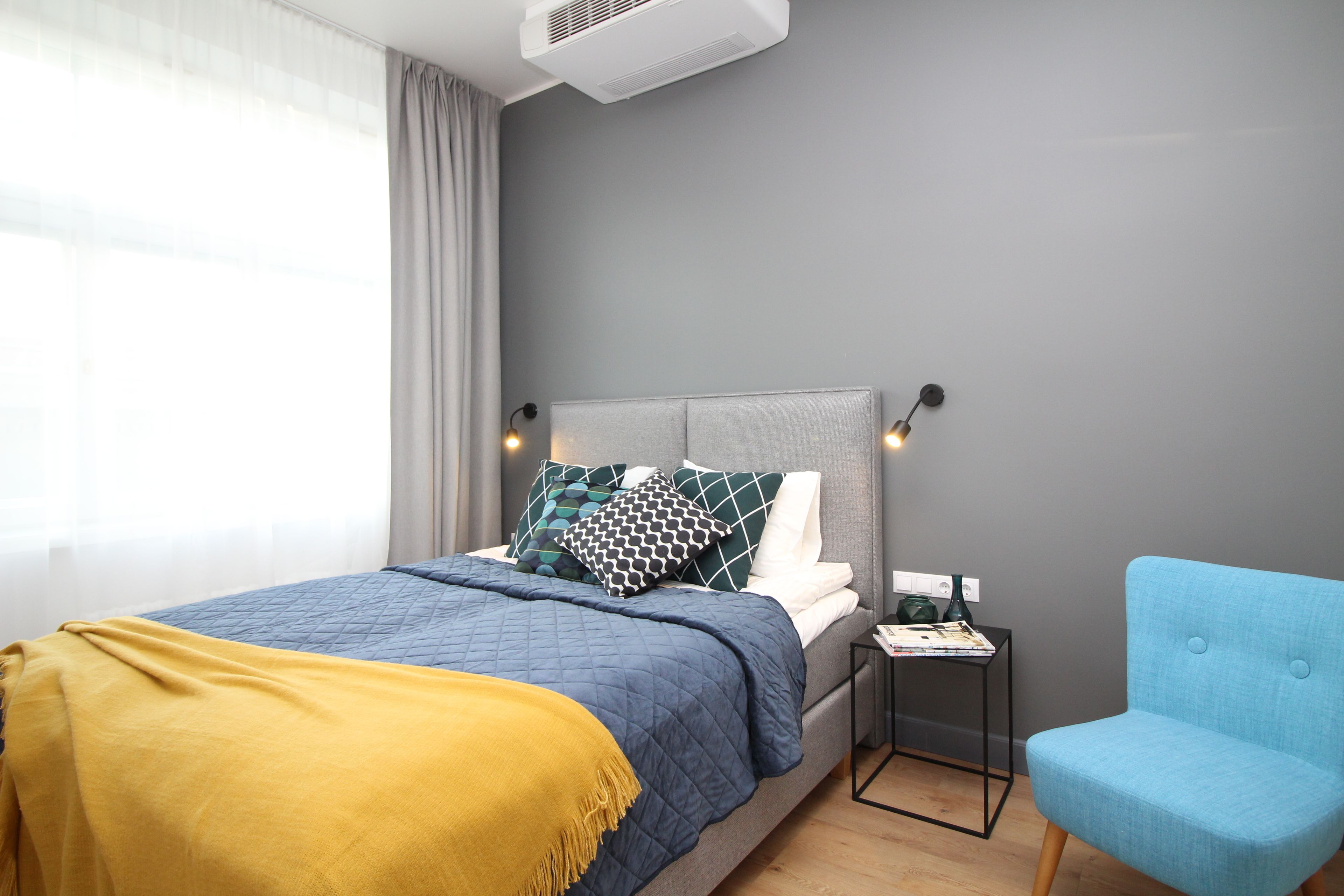A modern bedroom with a bed, a bedside table, a chair, and a window with curtains.