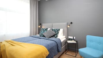 A modern bedroom with a bed, a bedside table, a chair, and a window with curtains.