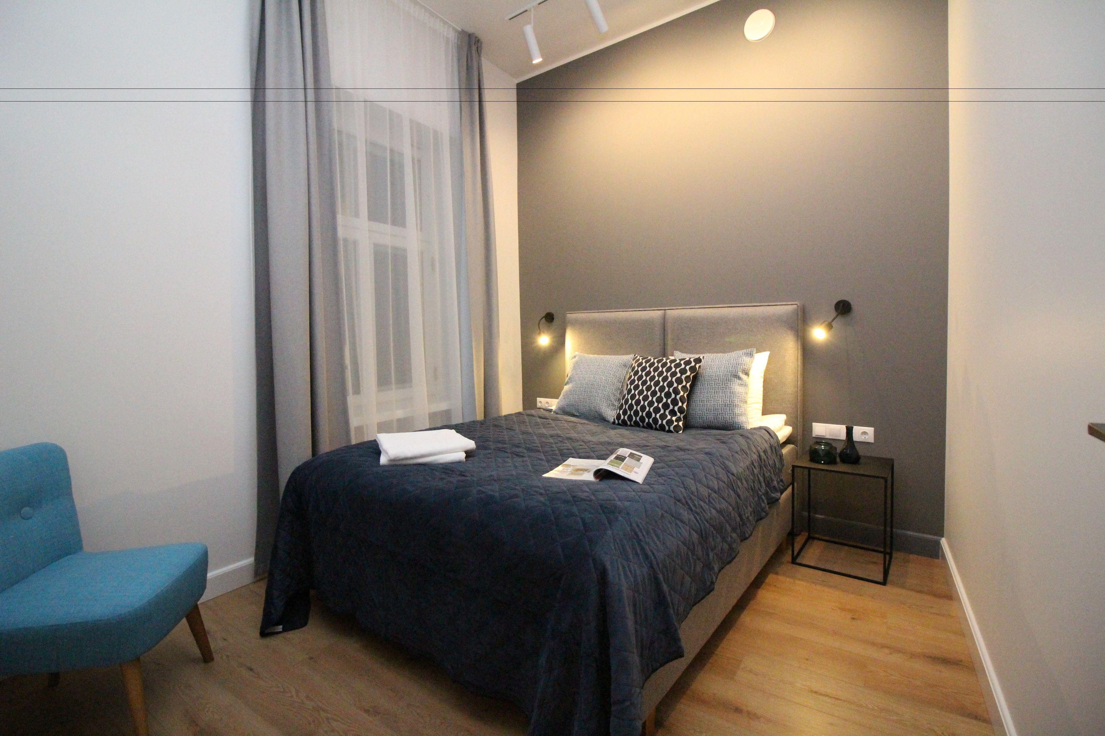 Een moderne slaapkamer met een bed, een nachtkastje, een stoel en een raam met gordijnen.