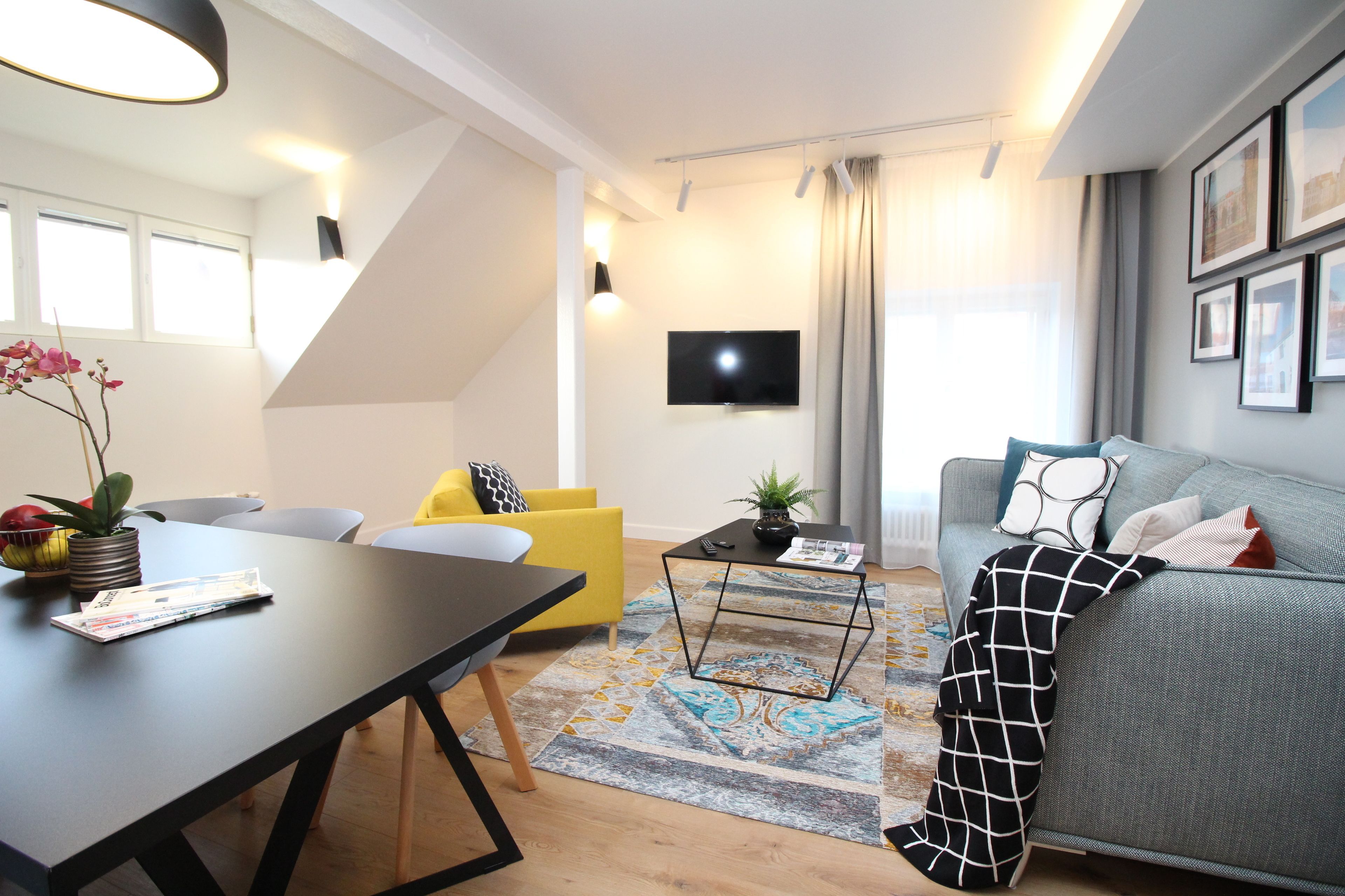 A modern living room with a sofa, a yellow armchair, a coffee table, and a flat-screen TV mounted on the wall.