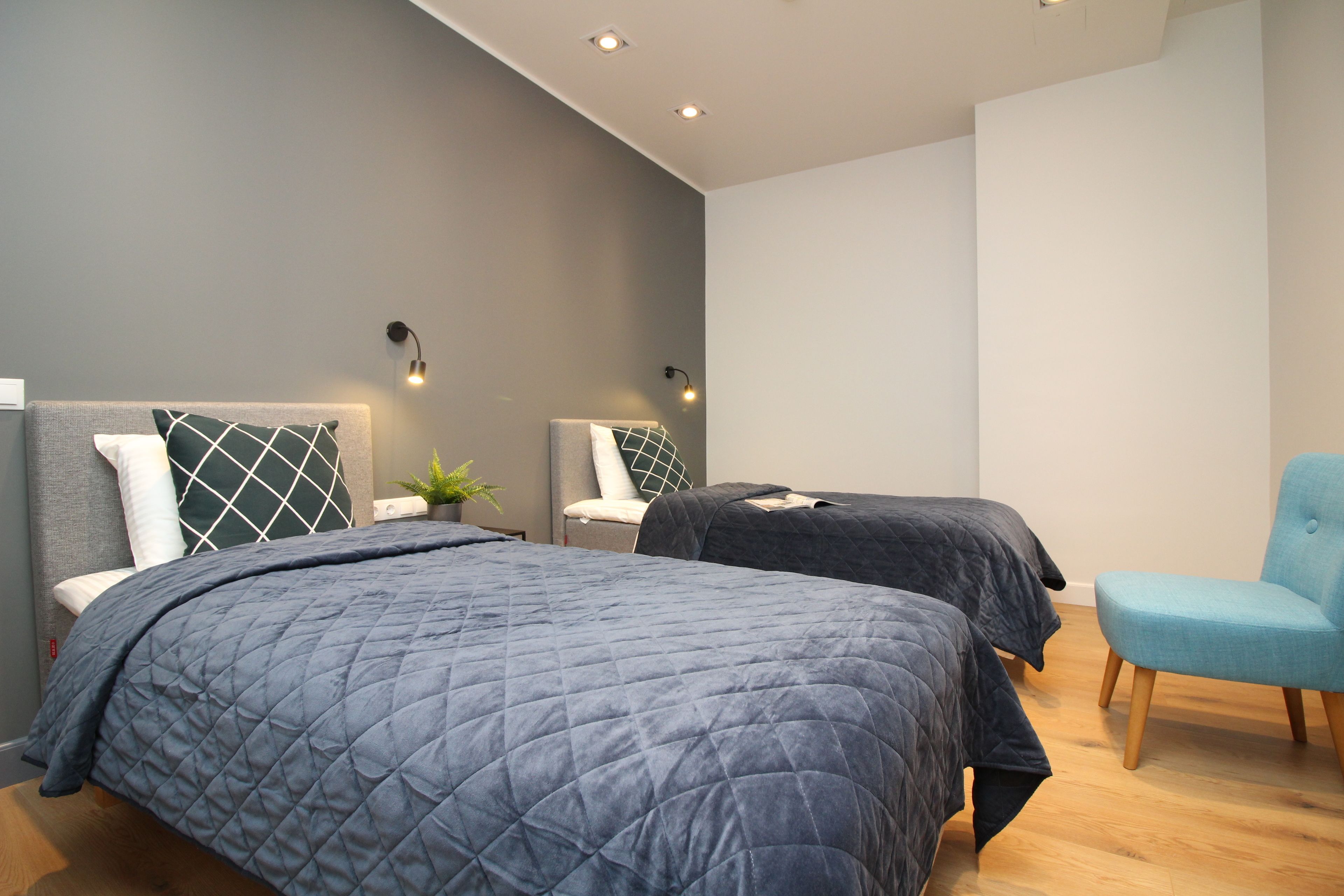 Ein modernes Schlafzimmer mit zwei Betten, einem blauen Sessel und einer kleinen Pflanze.