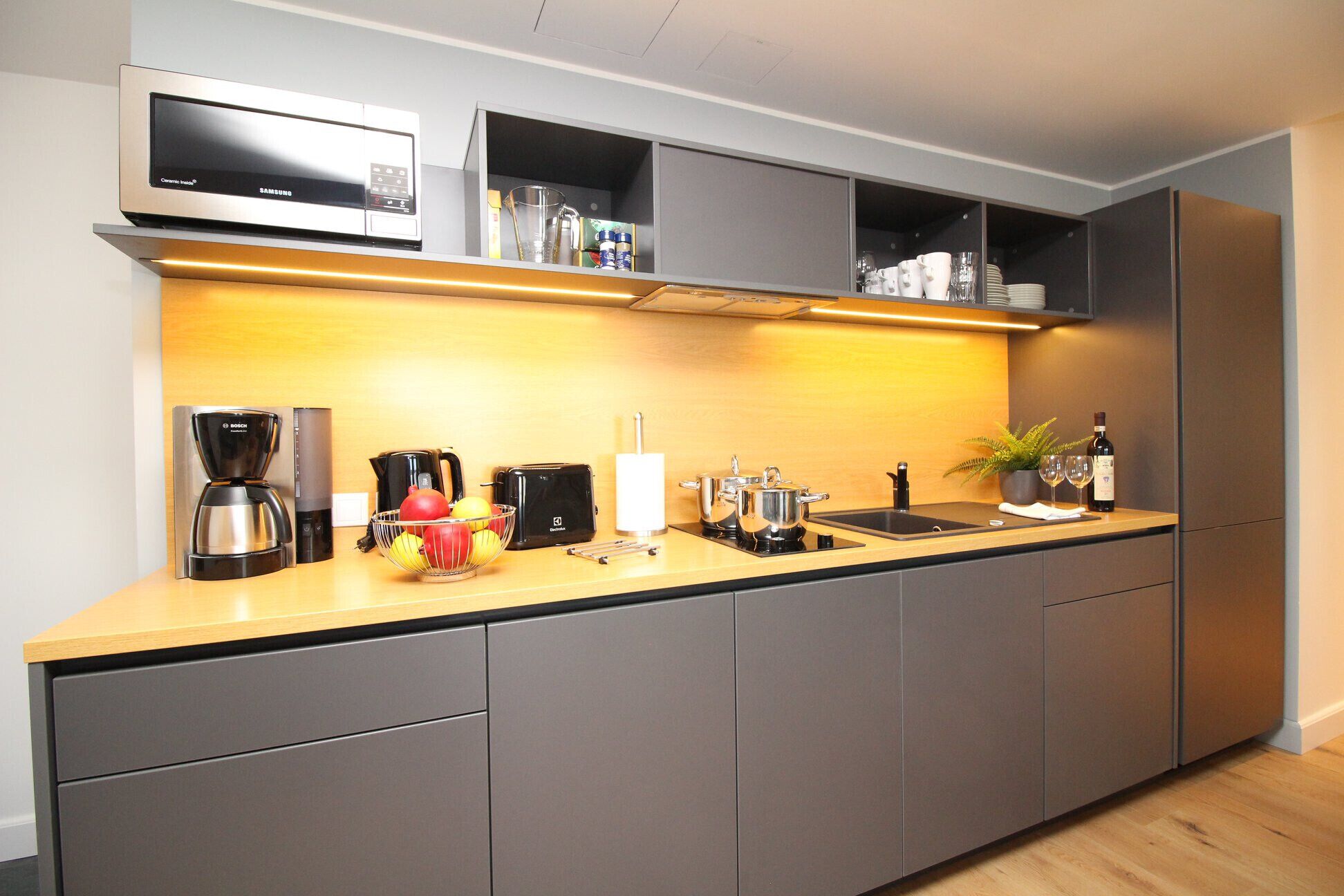 A modern kitchen with grey cabinets, a stainless steel Bosch coffee maker, a microwave, and a wine bottle.