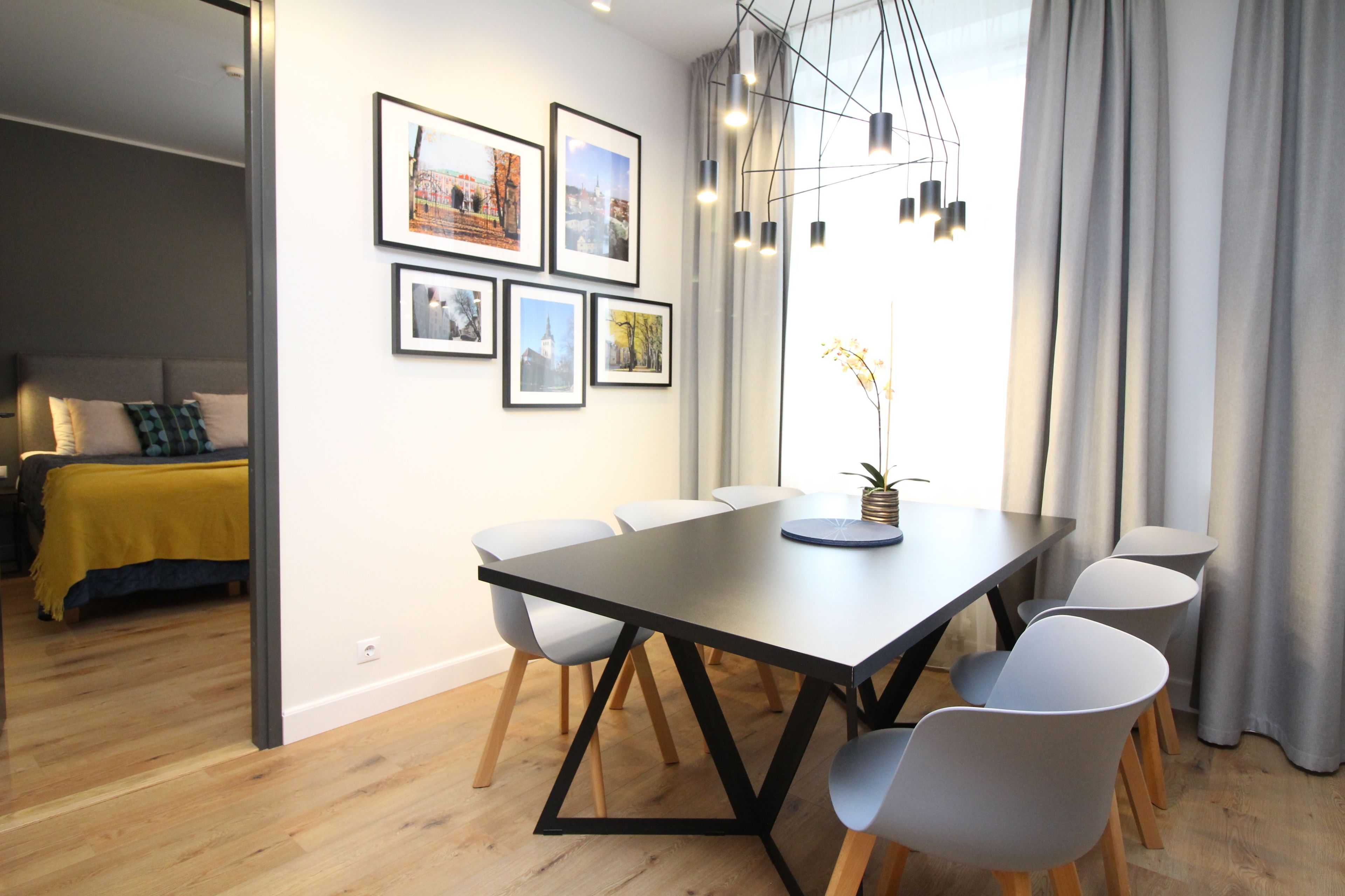 A modern dining area with a long table, six chairs, and a chandelier.