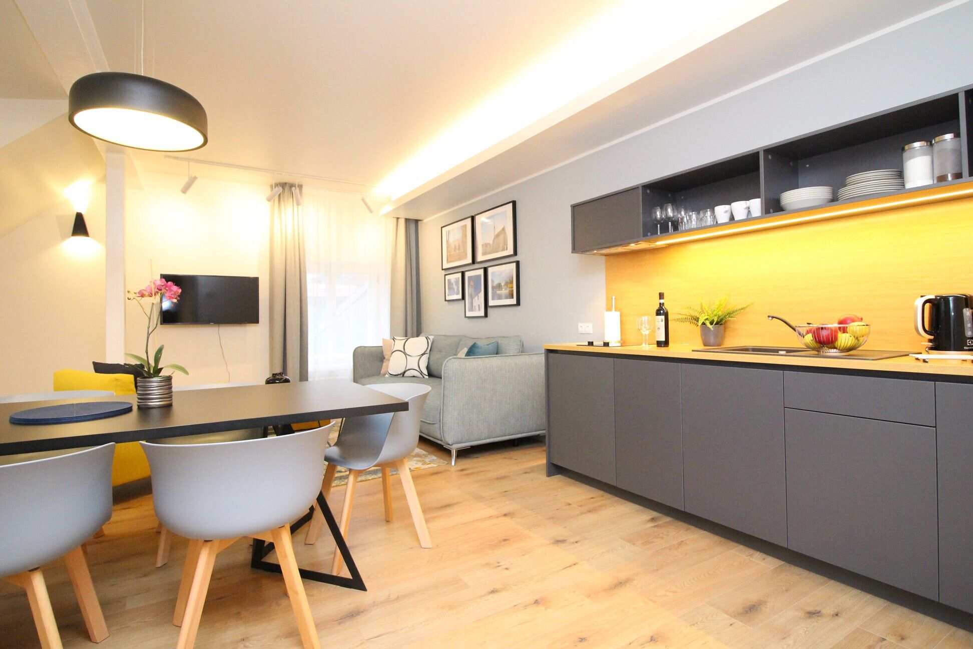 A modern kitchen with grey cabinets, a dining area with a table and chairs, and a grey sofa.