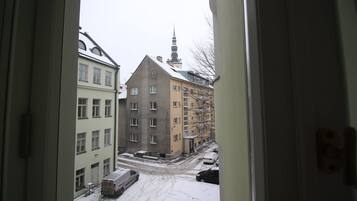 Een uitzicht door een open deur op een besneeuwde stadstraat, met gebouwen en een kerktoren op de achtergrond.