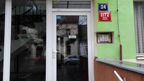 Een gevel met glazen deur, een metalen luifel en een groene wand met een bord waarop nummer 24 en adres 1172 staat.