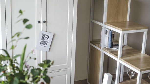 Een witte kast met een briefje, een houten boekenkast en een potplant.