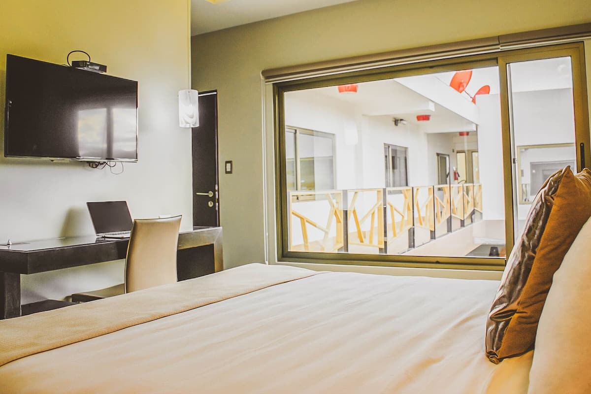 A hotel room with a bed, a desk with a laptop, a TV, and a balcony with a railing.