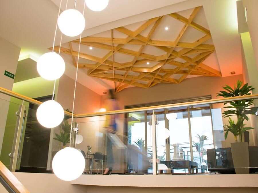 A modern interior with a wooden ceiling design, glass railings, and indoor plants.