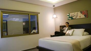 Una habitació d'hotel amb un llit, una finestra que ofereix vistes a l'exterior, una làmpada penjada a la paret i un objecte decoratiu sobre el llit.