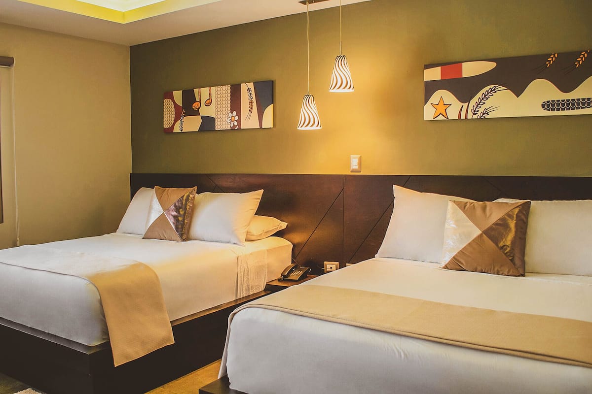 A hotel room with two beds, a window with a view of a building, and artwork on the wall.