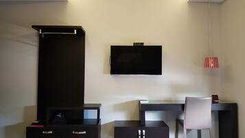 A modern room with a flat-screen TV mounted on the wall, a desk with a chair, and a small cabinet with drawers.