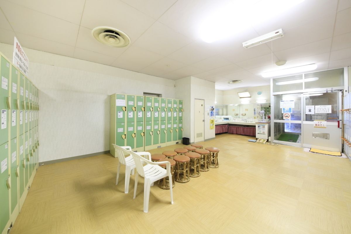 A room with green lockers, white chairs, and a counter with a refrigerator.