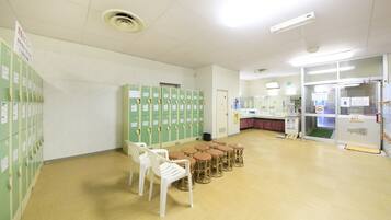 A room with green lockers, white chairs, and a counter with a refrigerator.