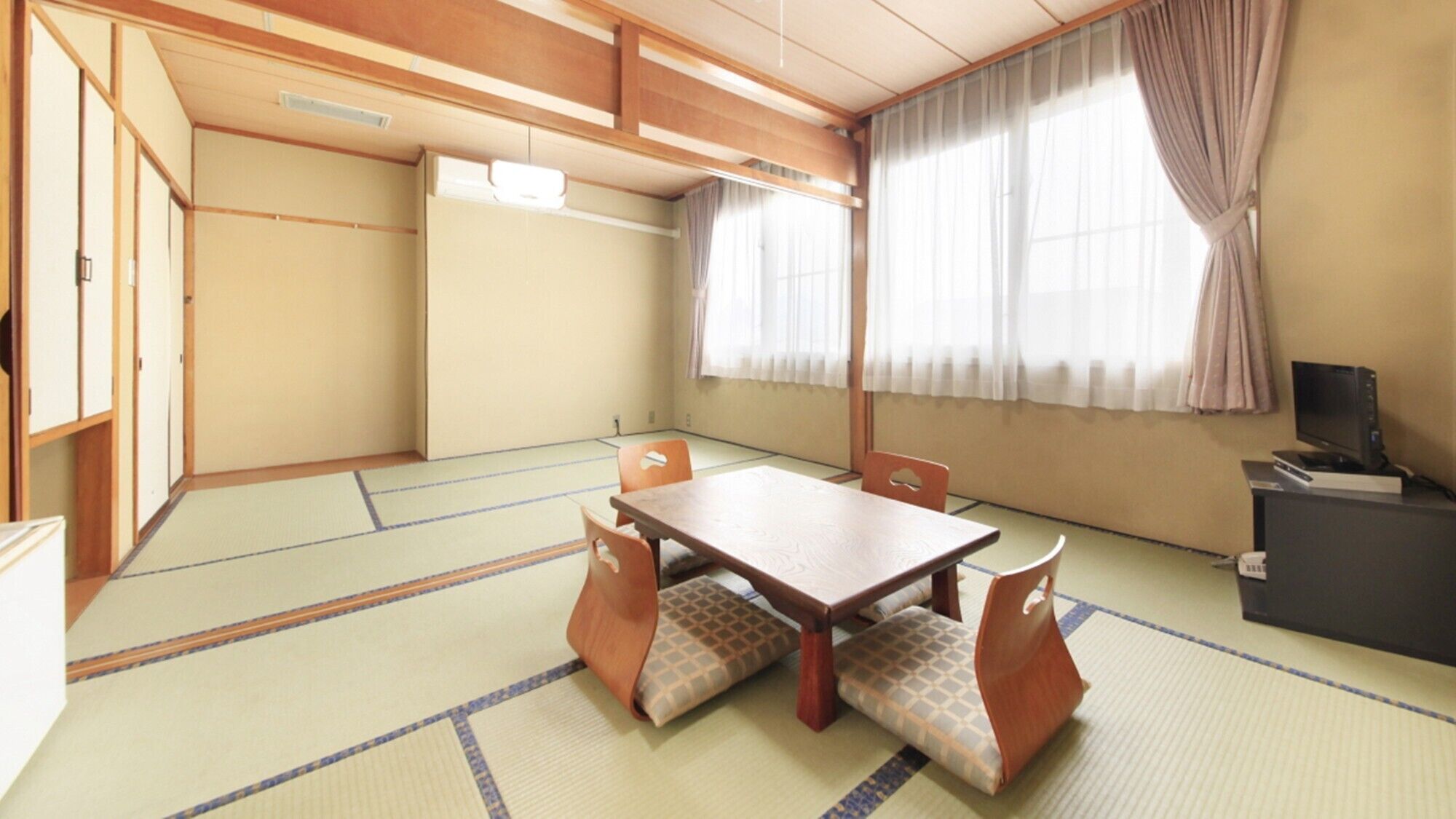 Una habitación tradicional japonesa con suelo de tatami, una mesa baja con cojines, un televisor sobre un mueble y puertas correderas.
