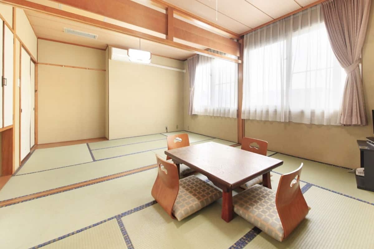 A traditional Japanese room with tatami flooring, a low table with cushions, a television on a stand, and sliding doors.
