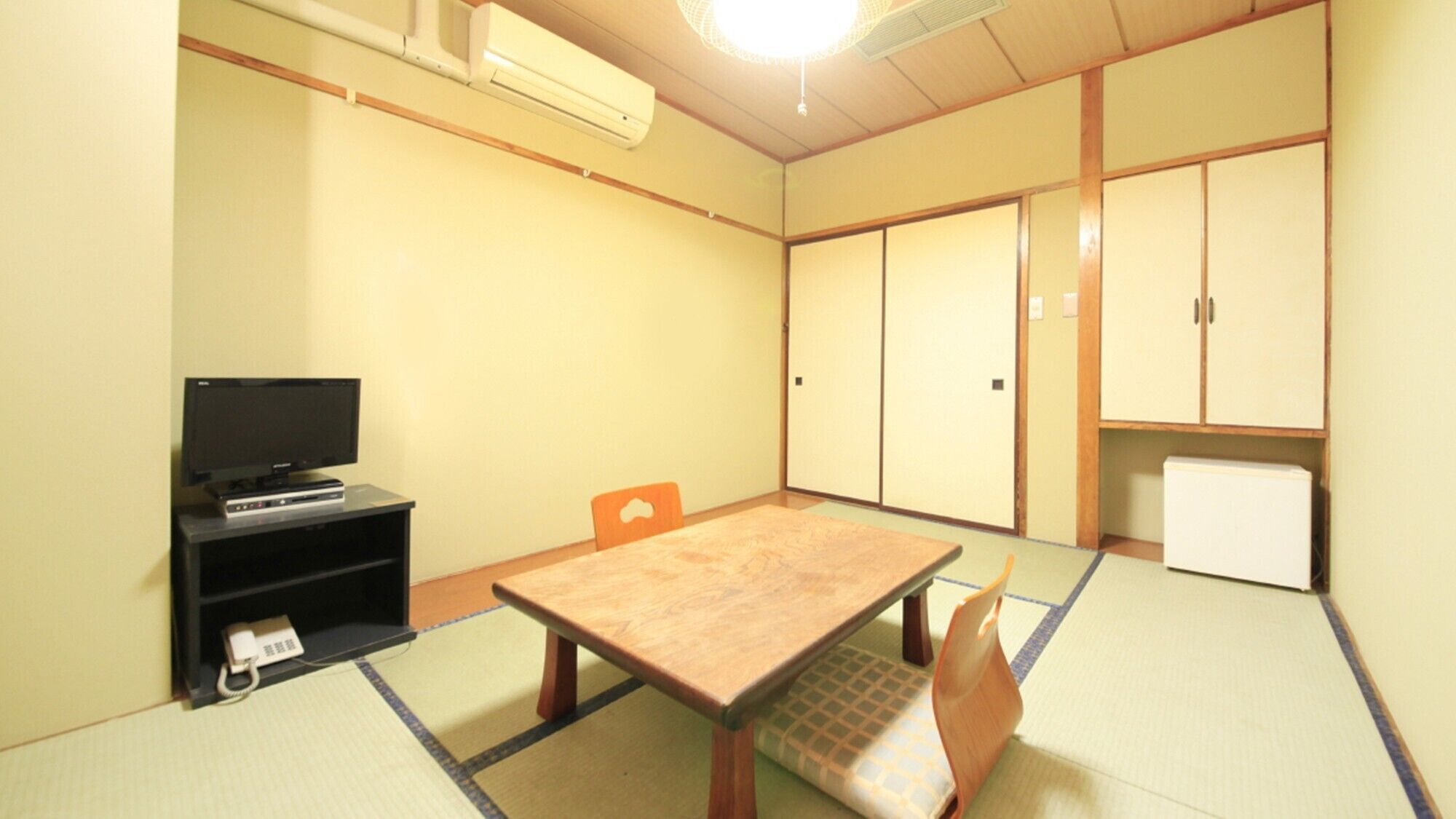 Una habitación con suelo de tatami, un televisor sobre un mueble, un armario y una puerta.