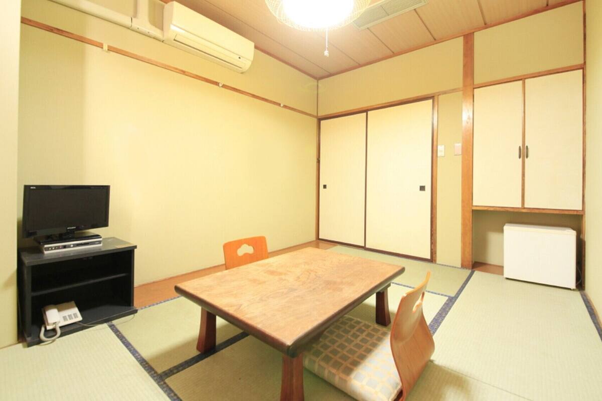 A room with tatami flooring, a television on a stand, a cabinet, and a door.