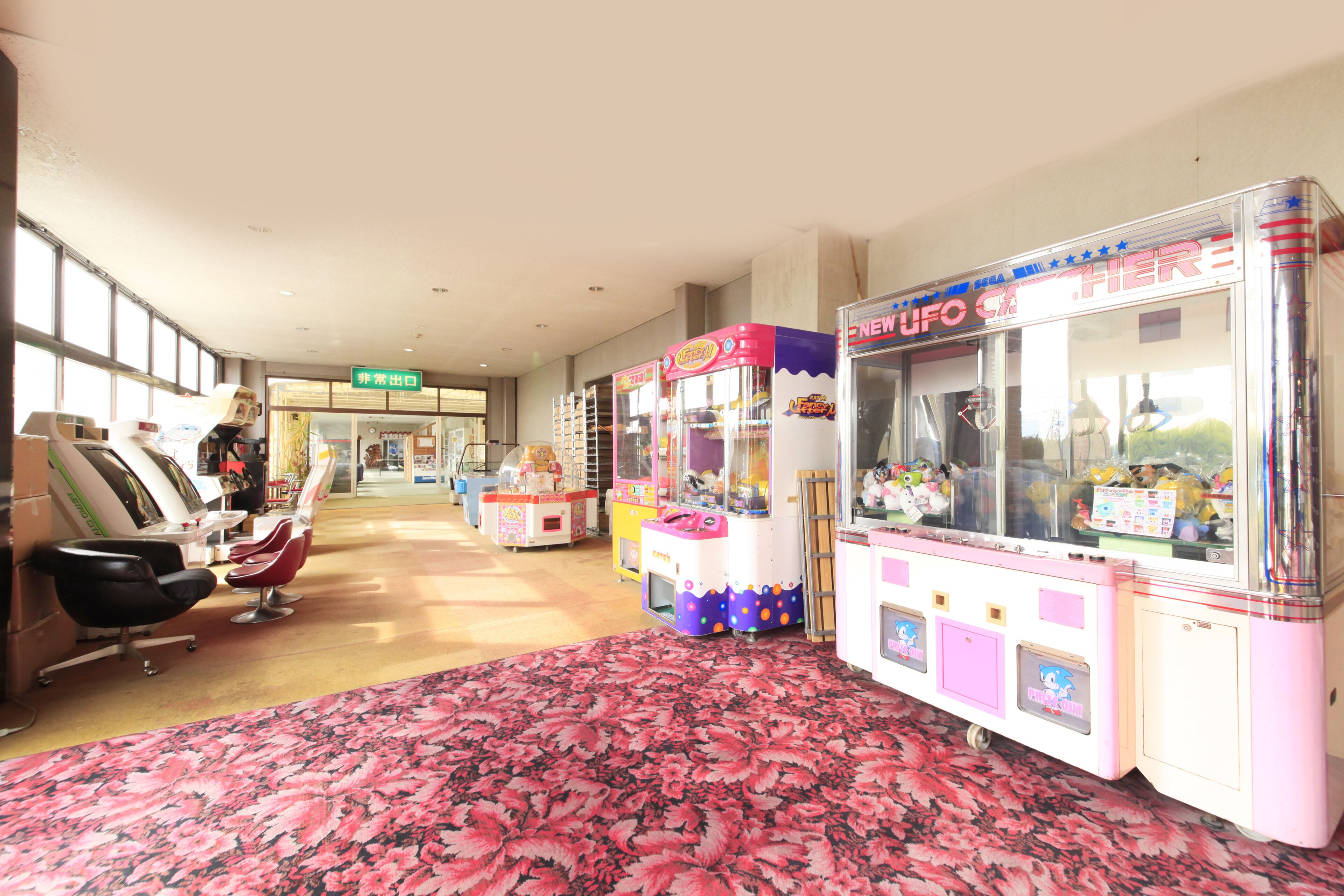A hotel lobby with a floral carpet, a salon area with chairs, and claw machines.