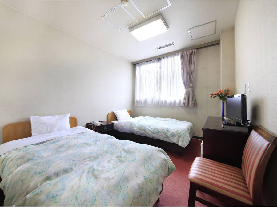 A hotel room with two beds, a desk, a chair, a TV, and a window with curtains.