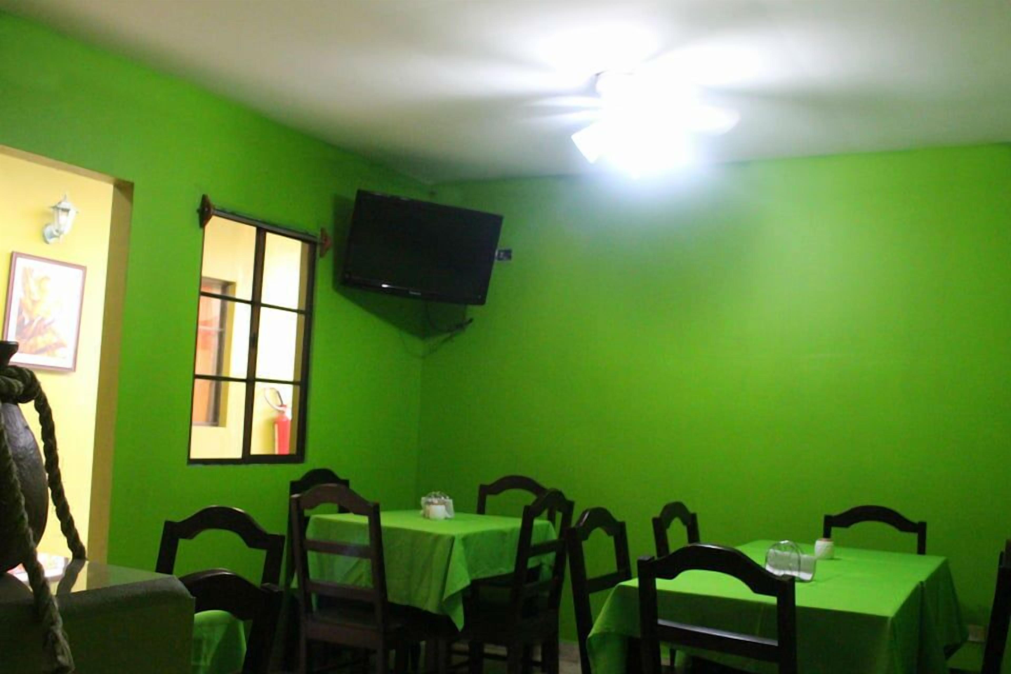 A room with green walls, a ceiling fan, a flat-screen TV mounted on the wall, and tables with chairs.