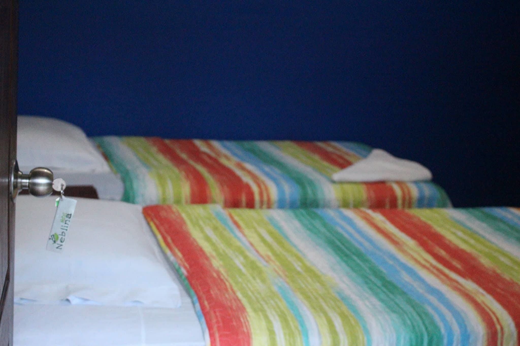 Een hotelkamer met twee bedden, elk voorzien van streepjesbeddengoed en een wit kussen.