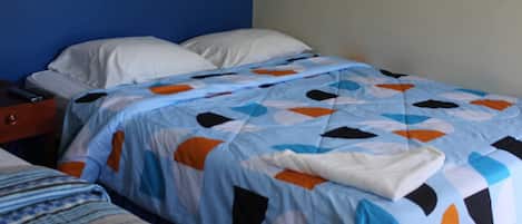 A bed with a blue and orange quilt, a white pillow, and a wooden nightstand with a remote control.