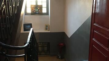 Una escalera con barandilla que conduce a una plataforma. Se observa una ventana con vistas al exterior, una puerta en la plataforma y un taburete pequeño.