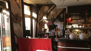 Un espace bar avec un coin salon rouge, un comptoir et diverses bouteilles et verres.
