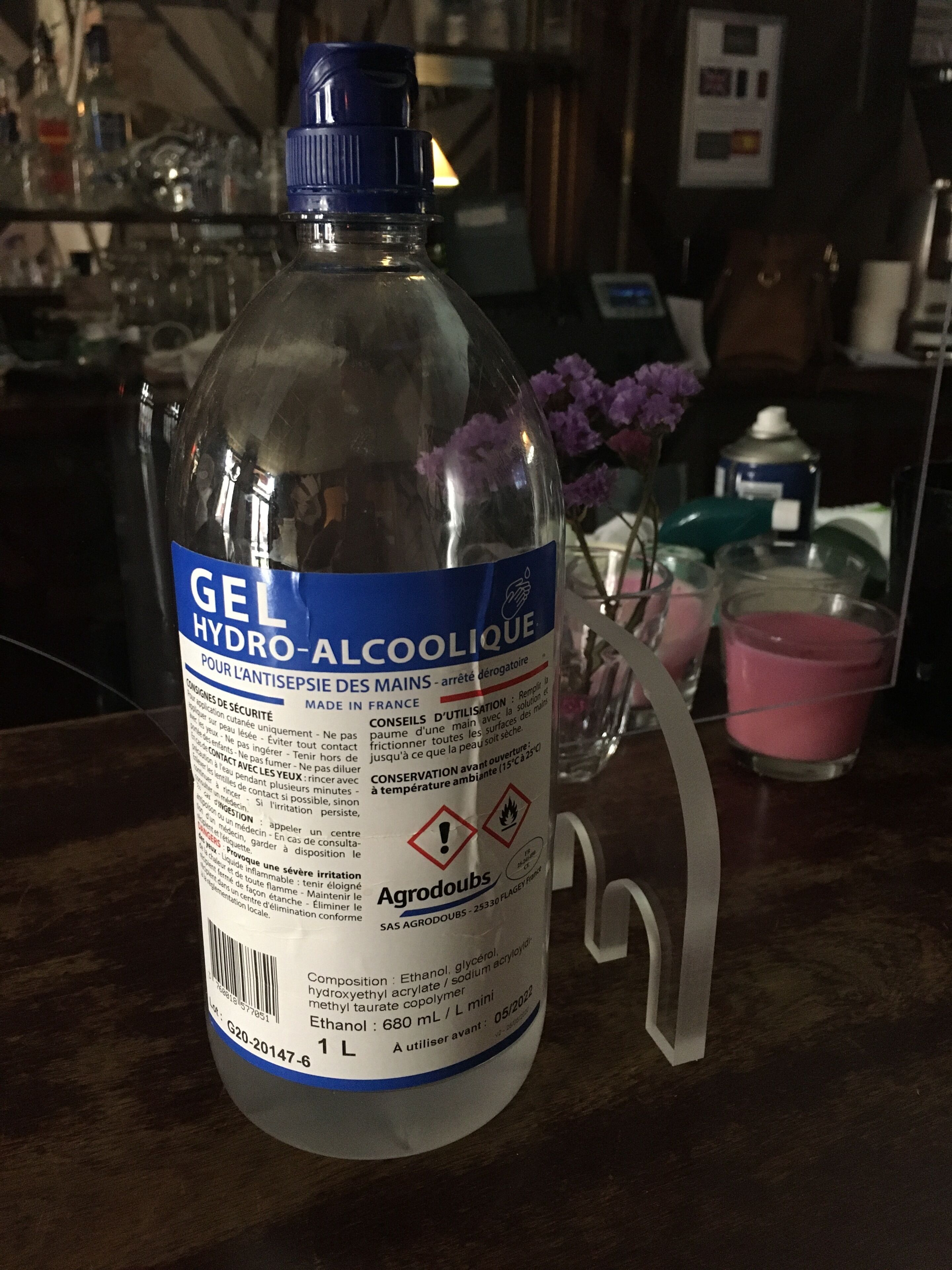 A bottle of gel hydro-alcoholique on a bar counter with a glass and pink candle in the background.