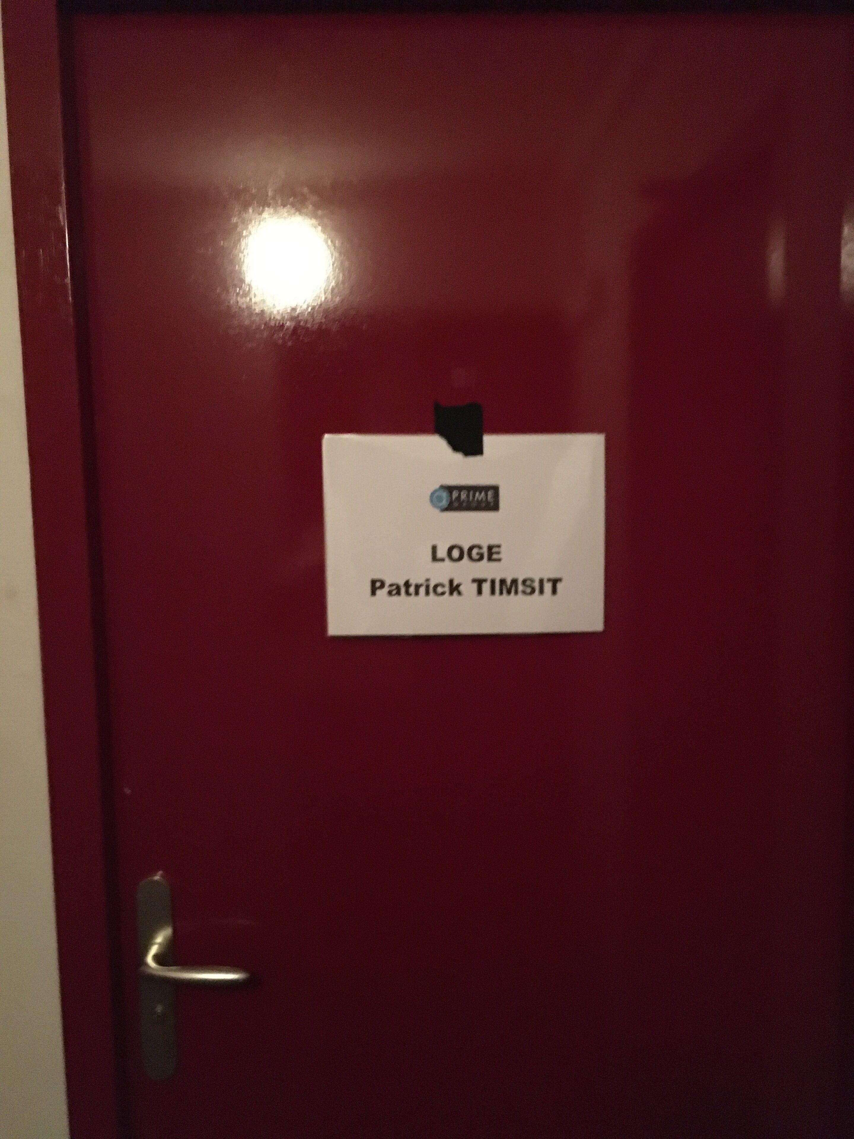 Eine rote Tür mit einem weißen Schild, auf dem "LOGE Patrick TIMSIT" steht.