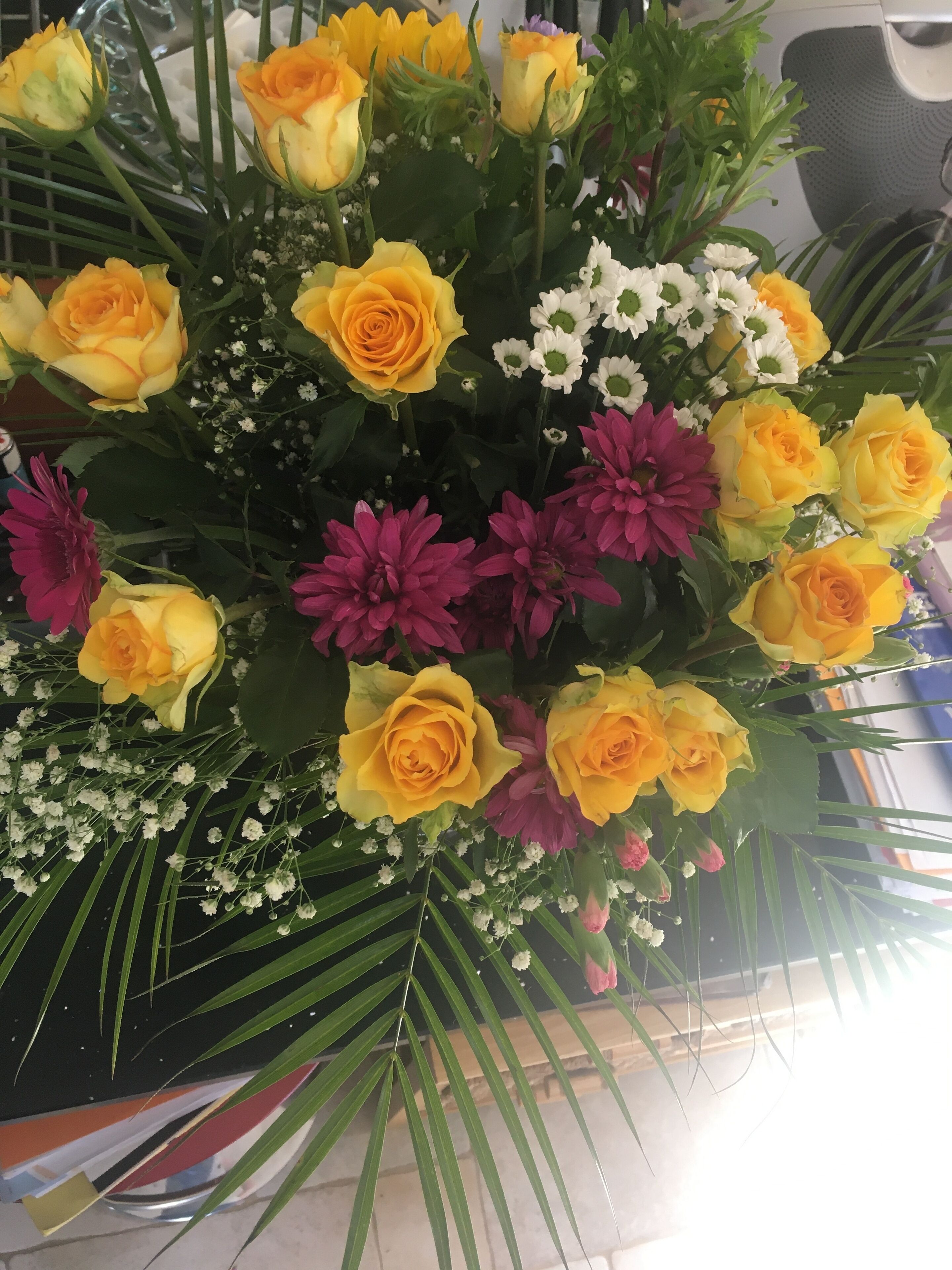 A bouquet of flowers with yellow roses, pink dahlias, and white daisies.