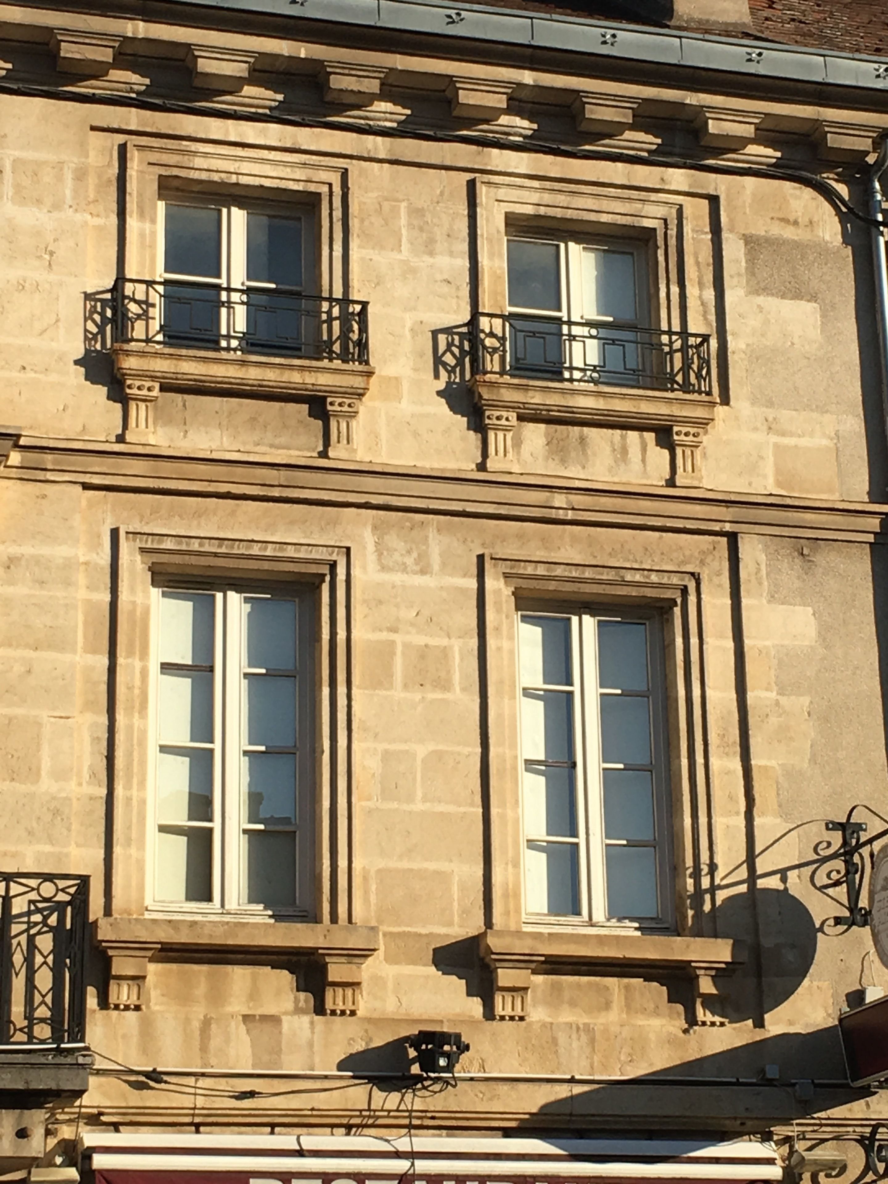 A building with three windows, each with a balcony. The building has a stone facade and decorative moldings.