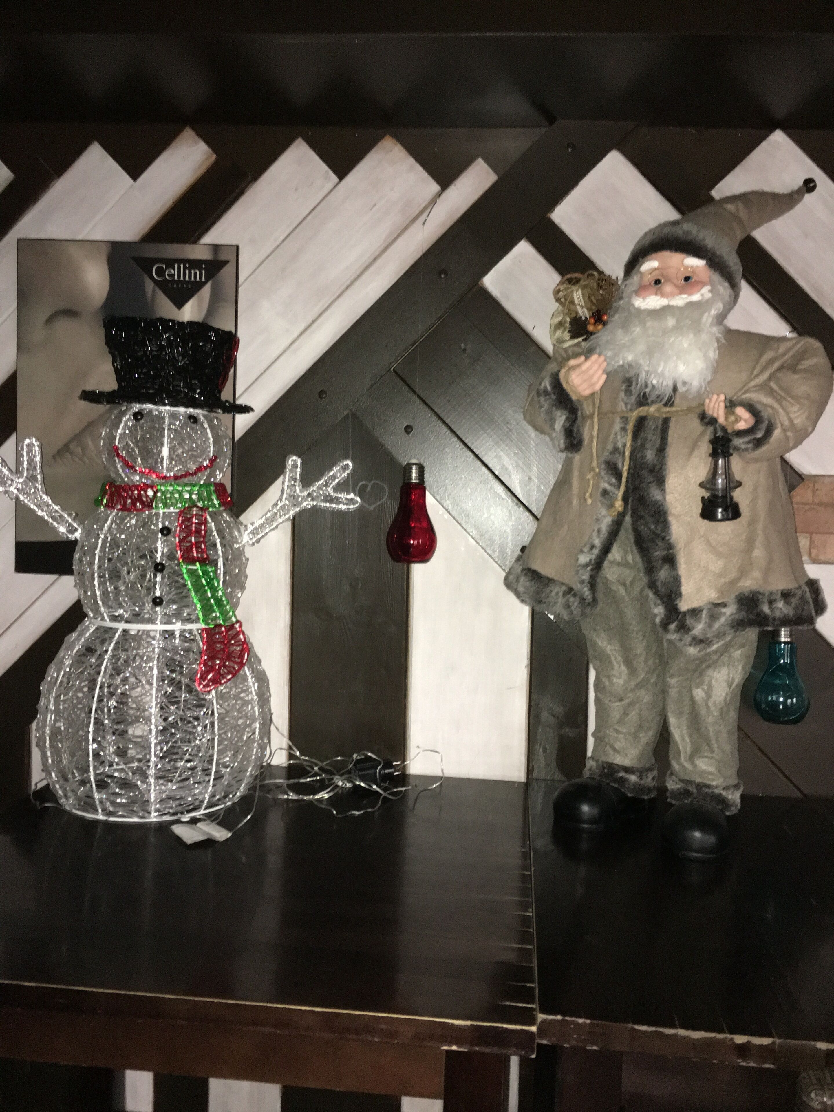 En snögubbe och en liten julgransprydnad formad som jultomte står på ett bord.