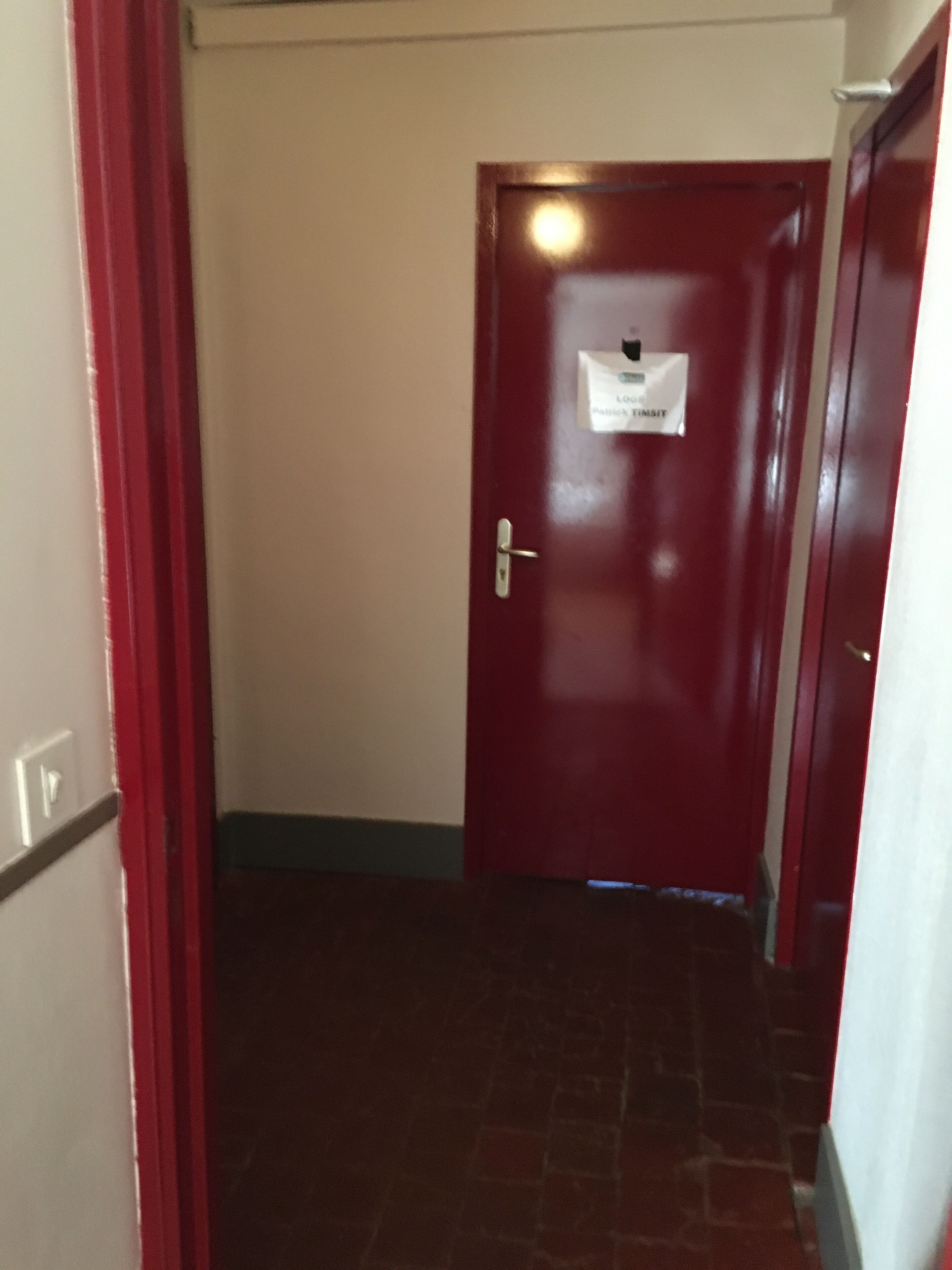 A narrow hallway with a red door, a sign on the door, and a light fixture above it.