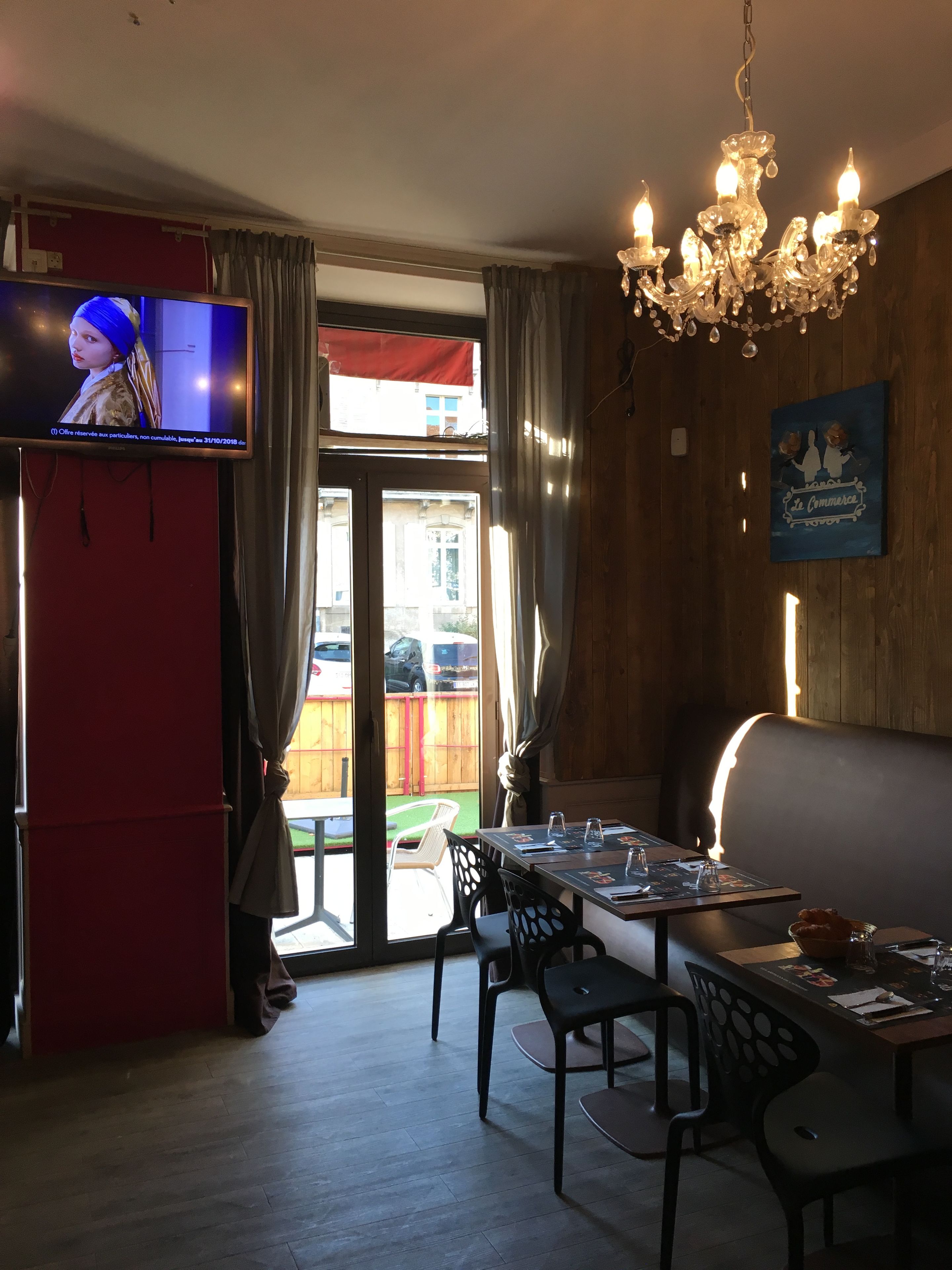 A restaurant with a TV, wooden walls, a chandelier, and a view of the street.