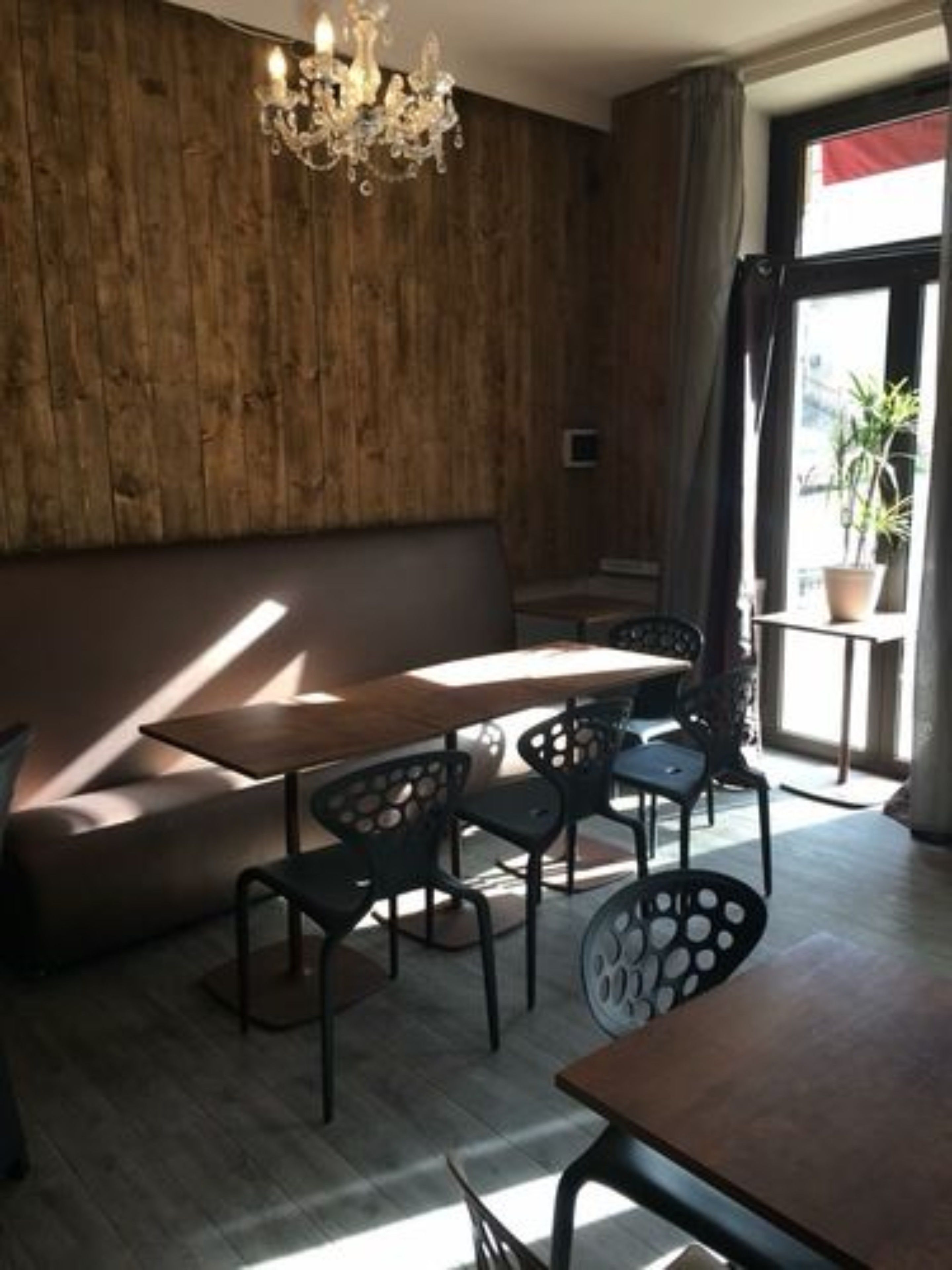 A cozy dining area with a wooden wall, a chandelier, and a window with curtains.