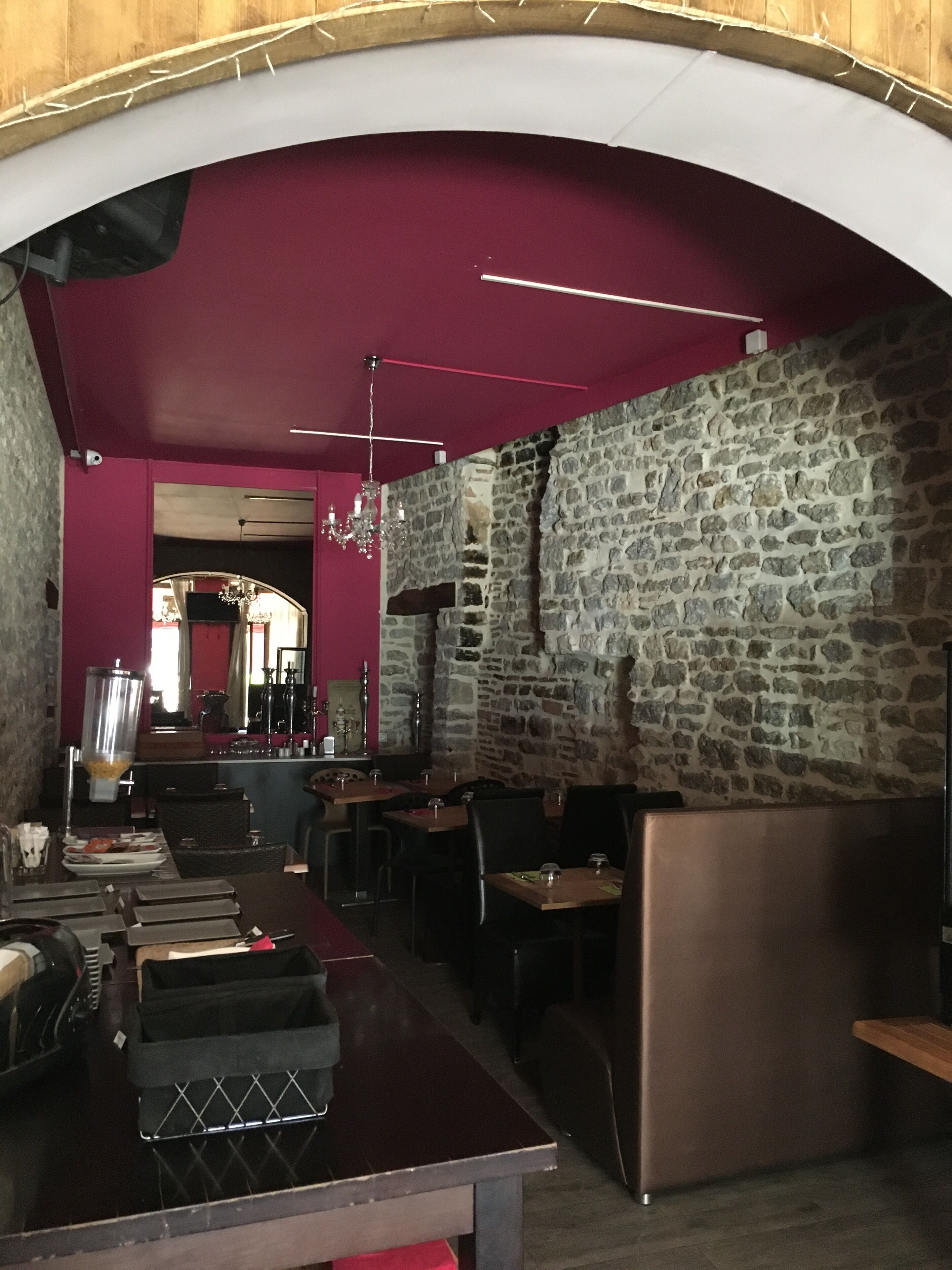 Un restaurante con paredes de piedra, techo de madera y paredes rojas. Mesas y sillas dispuestas para comer.