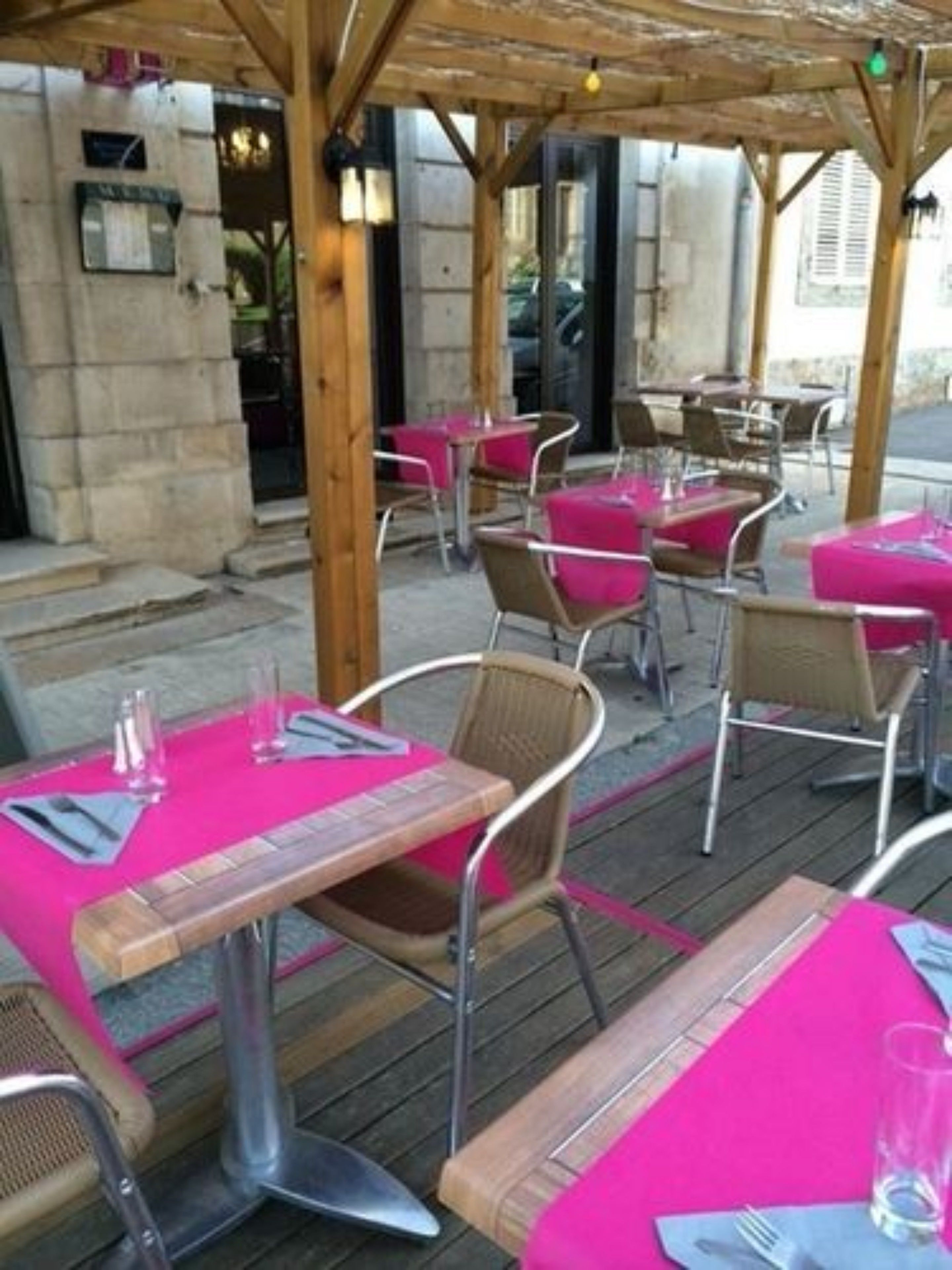 Un área de comedor al aire libre con mesas y sillas, cubierta por una pérgola de madera.